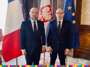 Marszałek Artur Kosicki pozuje do zdjęcia z gościem z Francji na tle flag Polski, Francji i UE